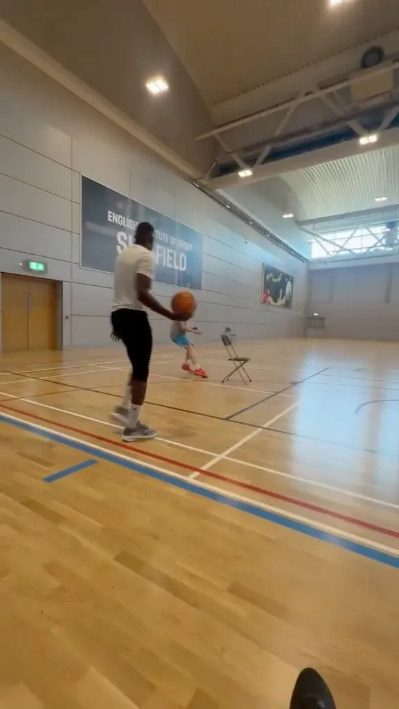 A coach and young people doing basketball drills in a large sports hall